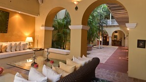 A spacious indoor area with a sofa, a glass coffee table, and a wicker chair. There are multiple arches and a balcony with a railing.