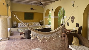 A hammock in a room with a stone floor, a sofa, a table, and a ceiling fan.