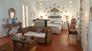 A cozy room with a wicker sofa, a bed with striped bedding, a desk with a lamp, and a wall decorated with star-shaped ornaments.