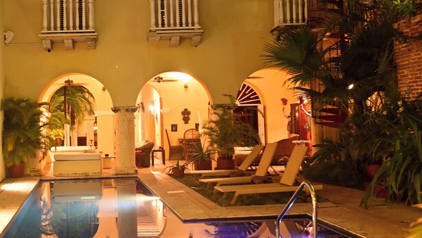 A pool area with lounge chairs, a reflection pool, and a building with arched windows and balconies.
