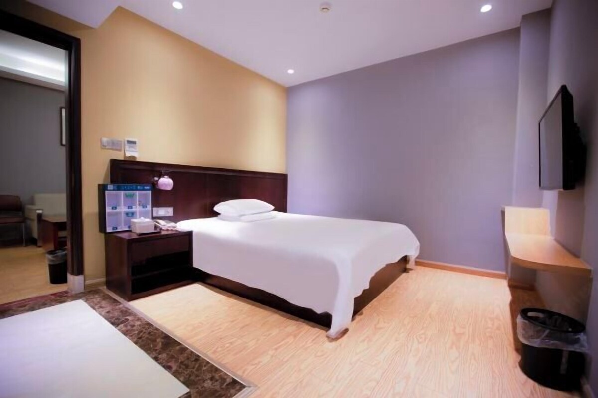 A hotel room with a bed, bedside table, lamp, and a TV mounted on the wall.