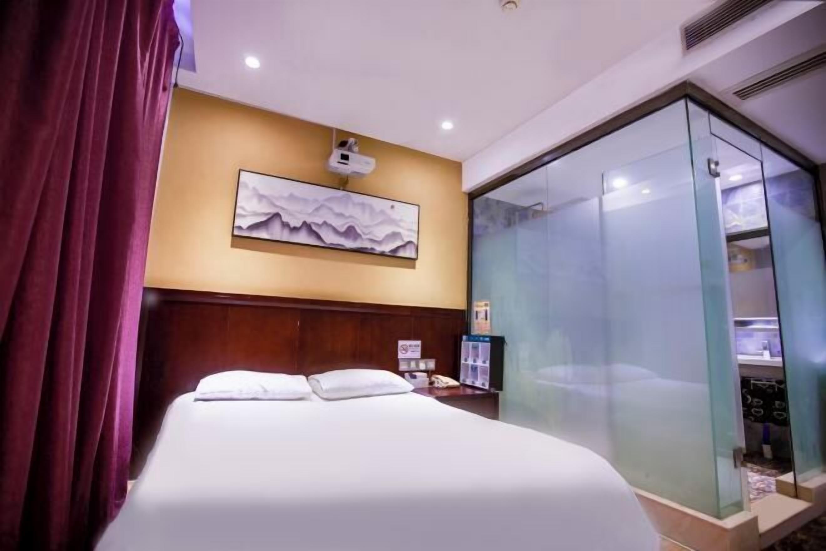 A hotel room with a bed, a nightstand, a glass-enclosed shower, and a wall-mounted projector.