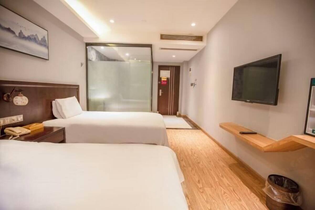 A hotel room with two beds, a TV, a phone, and a painting on the wall.