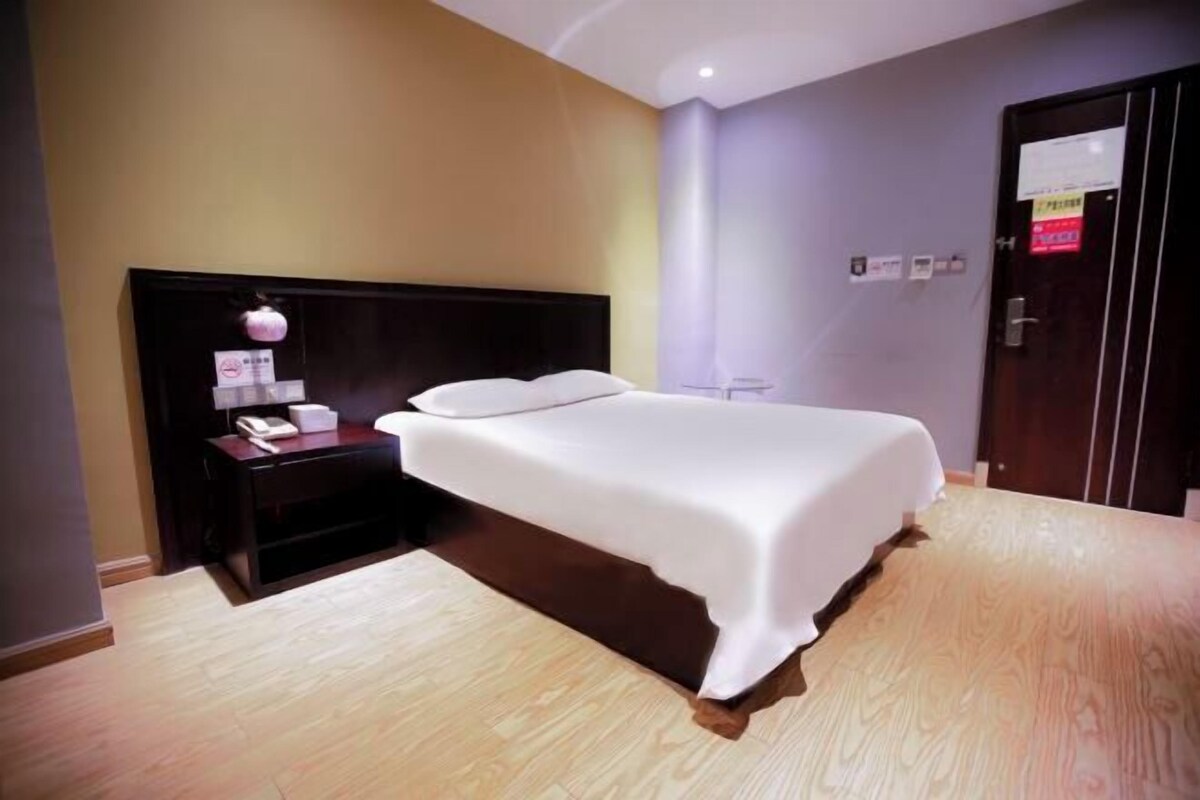 A hotel room with a bed, a nightstand, a lamp, and a door.