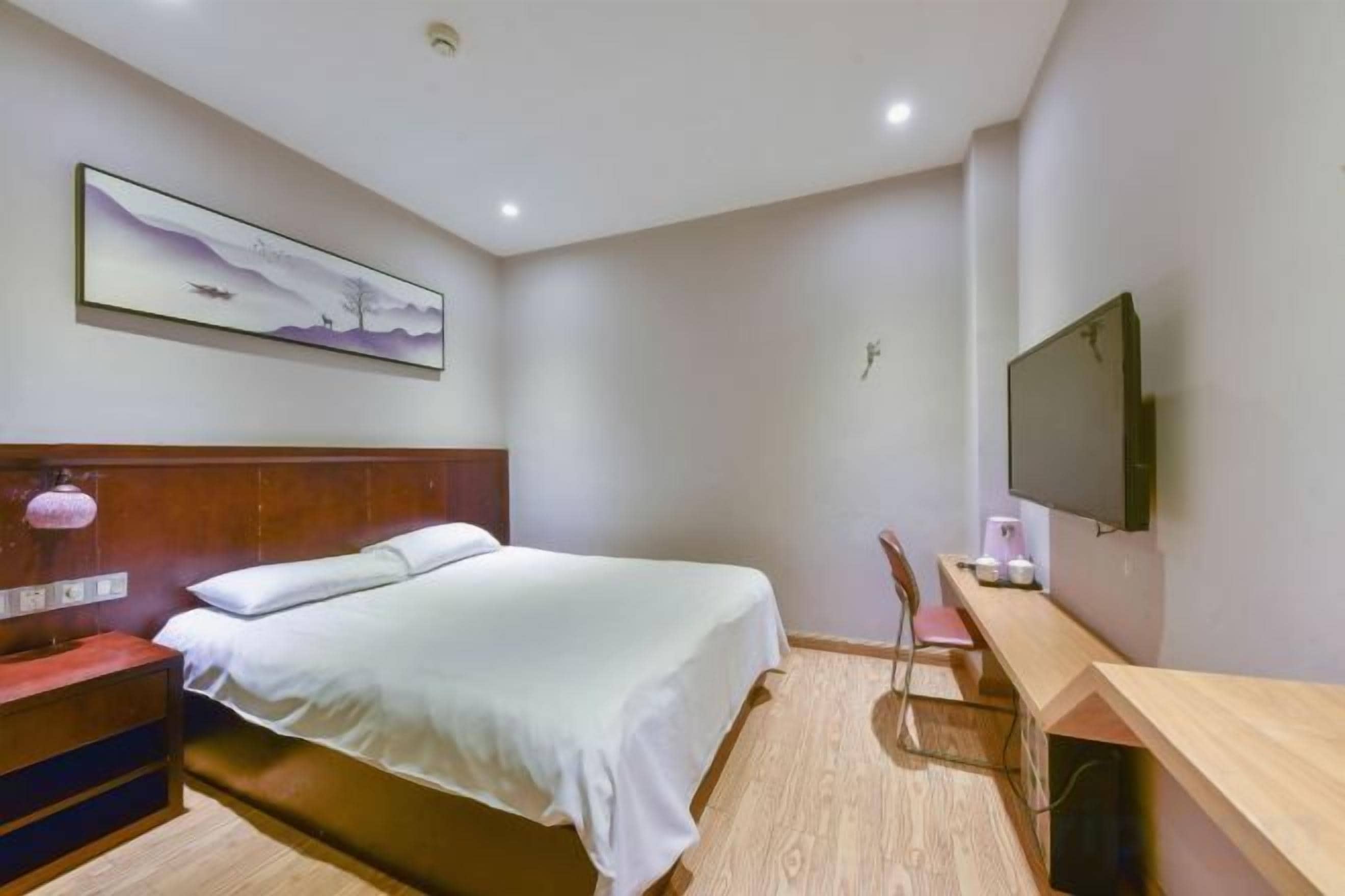 A hotel room with a bed, a desk, a chair, a TV, and a painting on the wall.