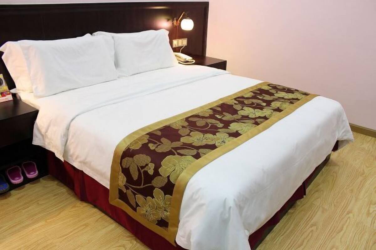 A bed with white linens, a floral-patterned bedspread, and a wooden nightstand with a lamp.