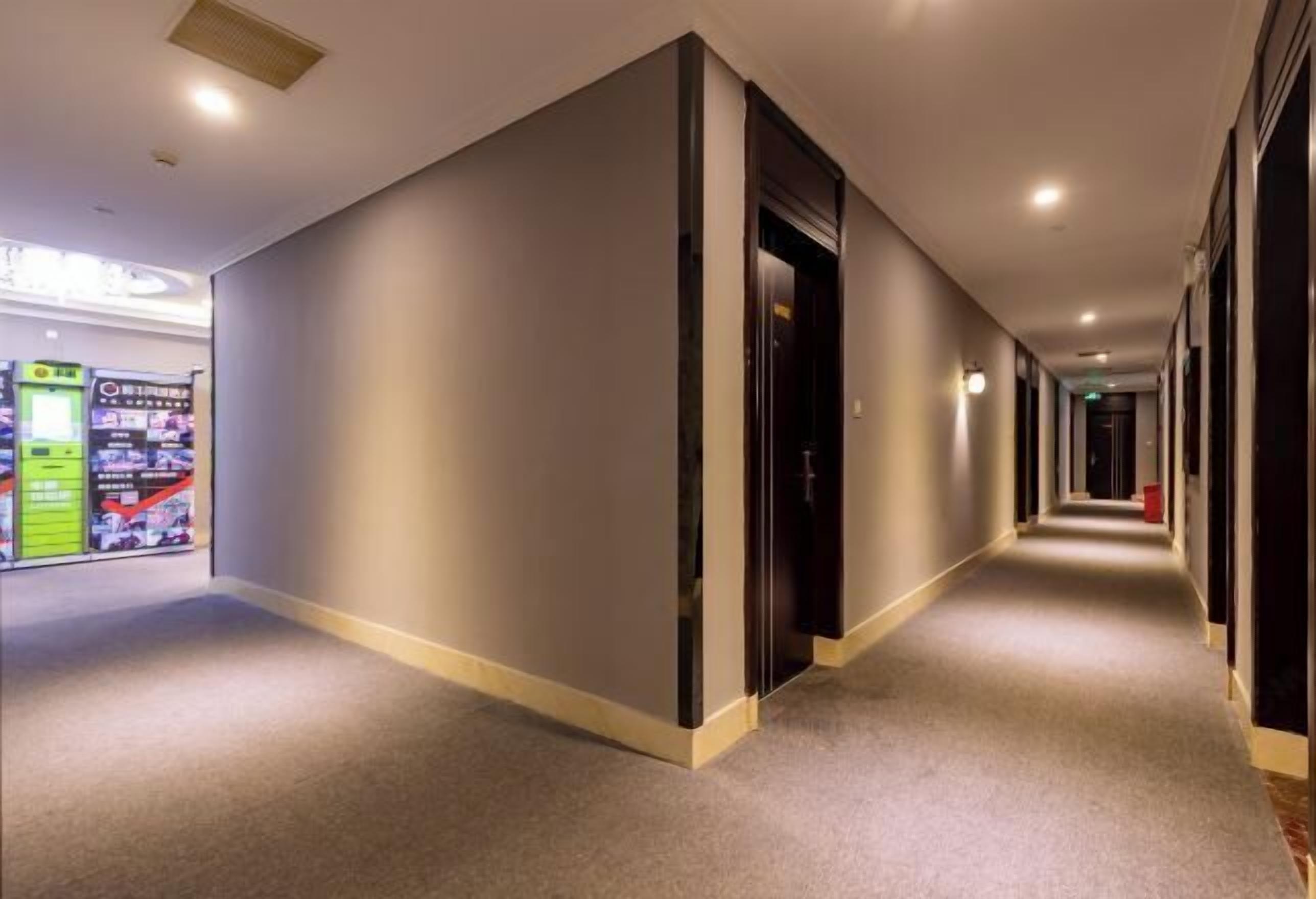 A hotel corridor with a carpeted floor, a vending machine on the left, and a door on the right.