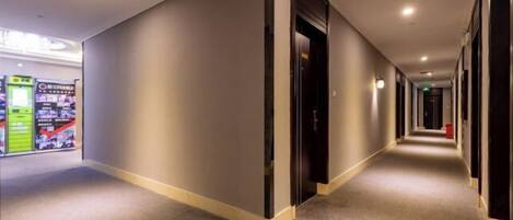 A hotel corridor with a carpeted floor, a vending machine on the left, and a door on the right.