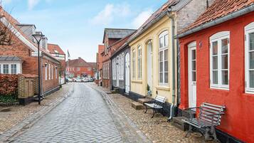 A cobblestone street lined with traditional buildings, a bench, and a red wall.