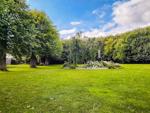 Un parc bien entretenu, avec une grande variété d’arbres, un parterre de fleurs central et un ciel dégagé.