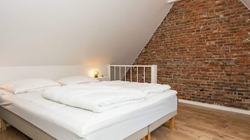Ein Schlafzimmer mit schrägverdeckter Decke, einer Ziegelwand und Holzboden.