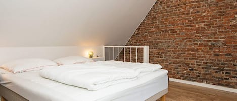 Une chambre avec un plafond en pente, un mur en briques et un plancher en bois.