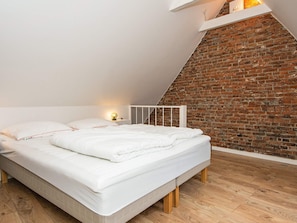A bedroom with a sloped ceiling, a brick wall, and a wooden floor.