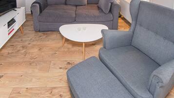 A living room with a grey sofa, a white coffee table, and a television on a white stand.