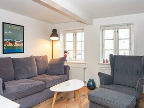 A living room with a grey sofa, a white coffee table, and a grey armchair. There is a framed picture on the wall and a window with a view of buildings. - 4 Person Holiday Home in Tonder-by Traum (Tonder)