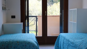 Ein Zimmer mit zwei Betten, einer Schiebetür, die auf einen Balkon führt, und einem weißen Schrank.
