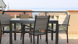 Ein Balkon mit Tisch und vier Stühlen, mit Blick auf eine Stadtlandschaft mit roten Dächern.