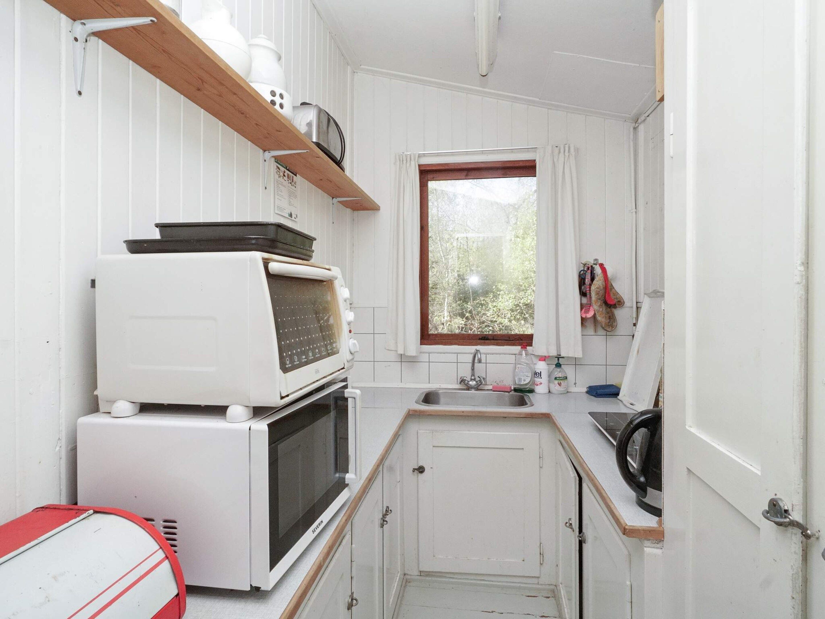 A compact kitchen with white cabinetry, a built-in microwave, a toaster, and a window with a view of greenery.