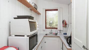 A compact kitchen with white cabinetry, a built-in microwave, a toaster, and a window with a view of greenery.
