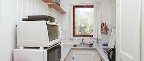 A compact kitchen with white cabinetry, a built-in microwave, a toaster, and a window with a view of greenery.