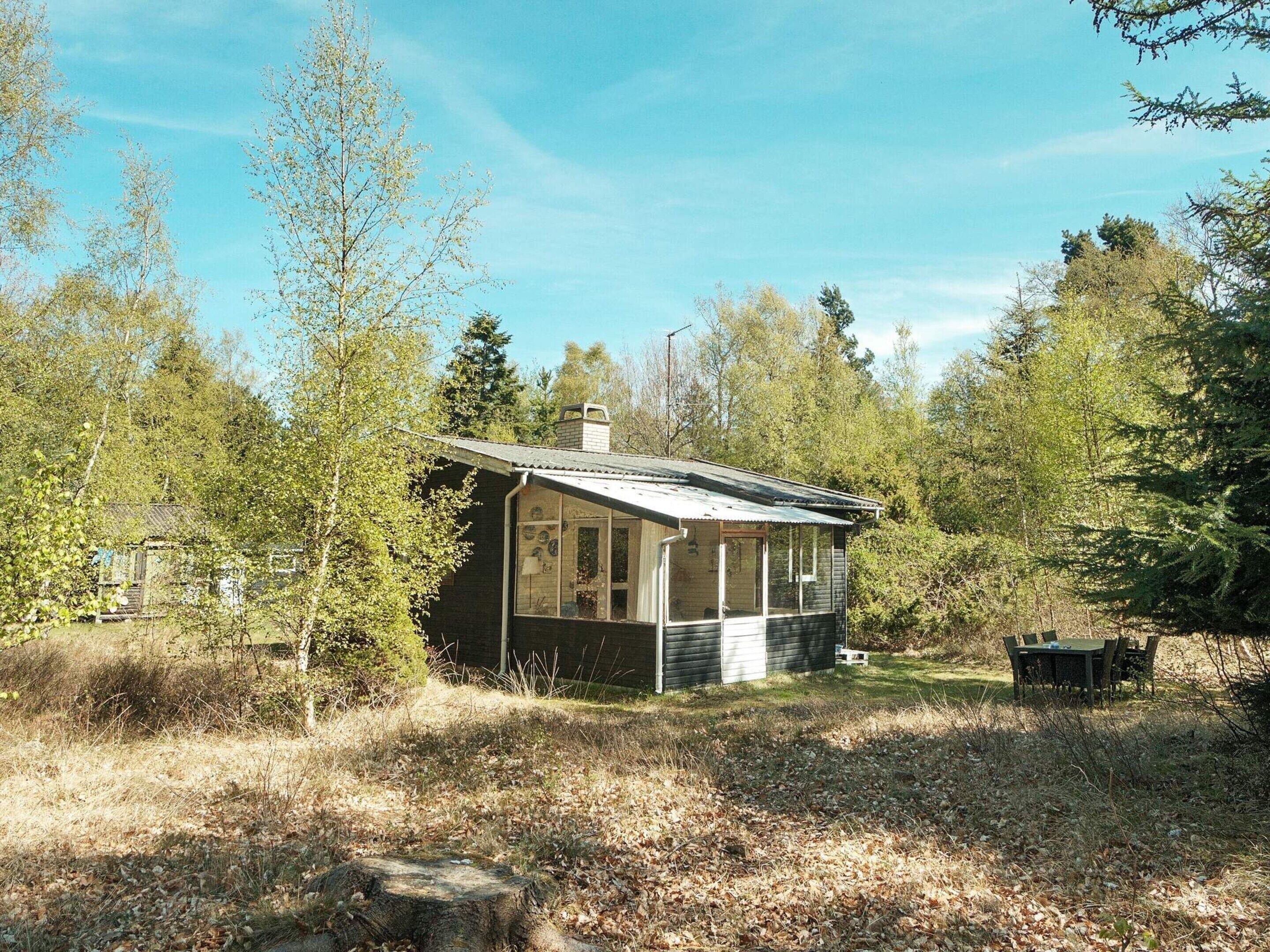 A small cabin with a porch, surrounded by trees and a grassy area.
