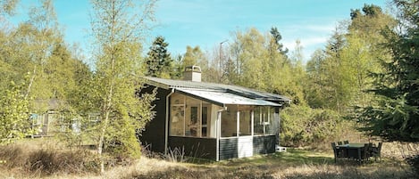 A small cabin with a porch, surrounded by trees and a grassy area.