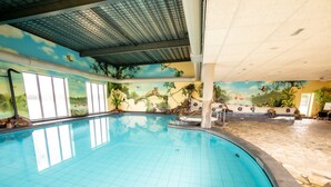 An indoor swimming pool with a mural of a tropical scene, clear blue water, and a tiled floor.