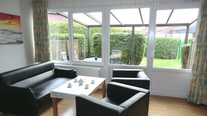 A living room with a sofa, two armchairs, and a table with teacups. Large windows offer a view of a garden and a house. - Lutje Carolinensiel Harlesiel (Wittmund)