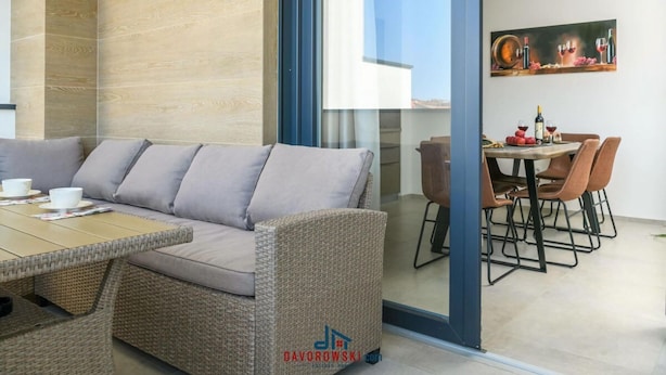 A modern living area with a sofa, wicker furniture, a dining table with chairs, and a glass partition. - Villa Dora - Apt 4 "bruin" (Pula)