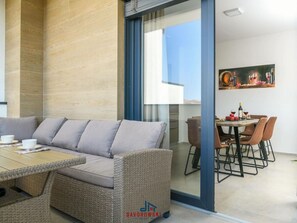 A modern living area with a sofa, wicker furniture, a dining table with chairs, and a glass partition. - Villa Dora - Apt 4 "bruin" (Pula)