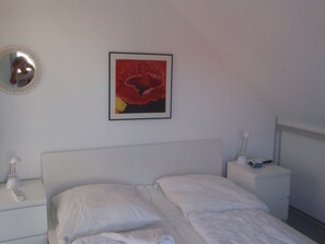 Un dormitorio con una cama, una mesita de noche con lámpara, una mesilla auxiliar y un cuadro enmarcado en la pared.