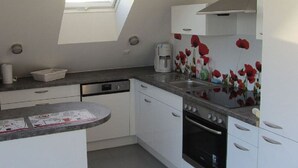Eine kleine Küche mit weißen Schränken, einem Backofen, einer Kaffeemaschine und einem Oberlicht.