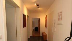 A narrow hallway with dark tiled flooring, a wooden bench, and a door on the left. - Cozy City Apartment (Essen)