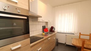 A modern kitchen with a built-in oven, a coffee machine, and a window with curtains. - Cozy City Apartment (Essen)