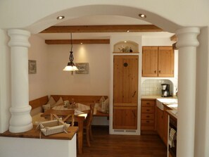 A cozy dining area with a wooden bench and table, a kitchen with wooden cabinets, and a hanging light fixture. - Hochkalter - Reich Family (Schoenau am Koenigssee)