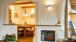 A cozy living room with a fireplace, wooden furniture, and a dining area visible through an archway. - Hochkalter - Reich Family (Schoenau am Koenigssee)