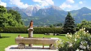 A wooden bench with a sculpture in a garden with a mountain backdrop. - Hochkalter - Reich Family (Schoenau am Koenigssee)