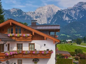 A traditional chalet with wooden balconies adorned with flower boxes, set against a backdrop of mountains. - Hochkalter - Reich Family (Schoenau am Koenigssee)