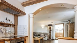 A spacious kitchen with wooden beams, a dining area with a sofa, and a large window. - Hochkalter - Reich Family (Schoenau am Koenigssee)