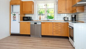 A kitchen with wooden cabinets, a dishwasher, a microwave, a stove, and a window with a view of greenery outside. - 6 Person Holiday Home in Nordborg (Nordborg)