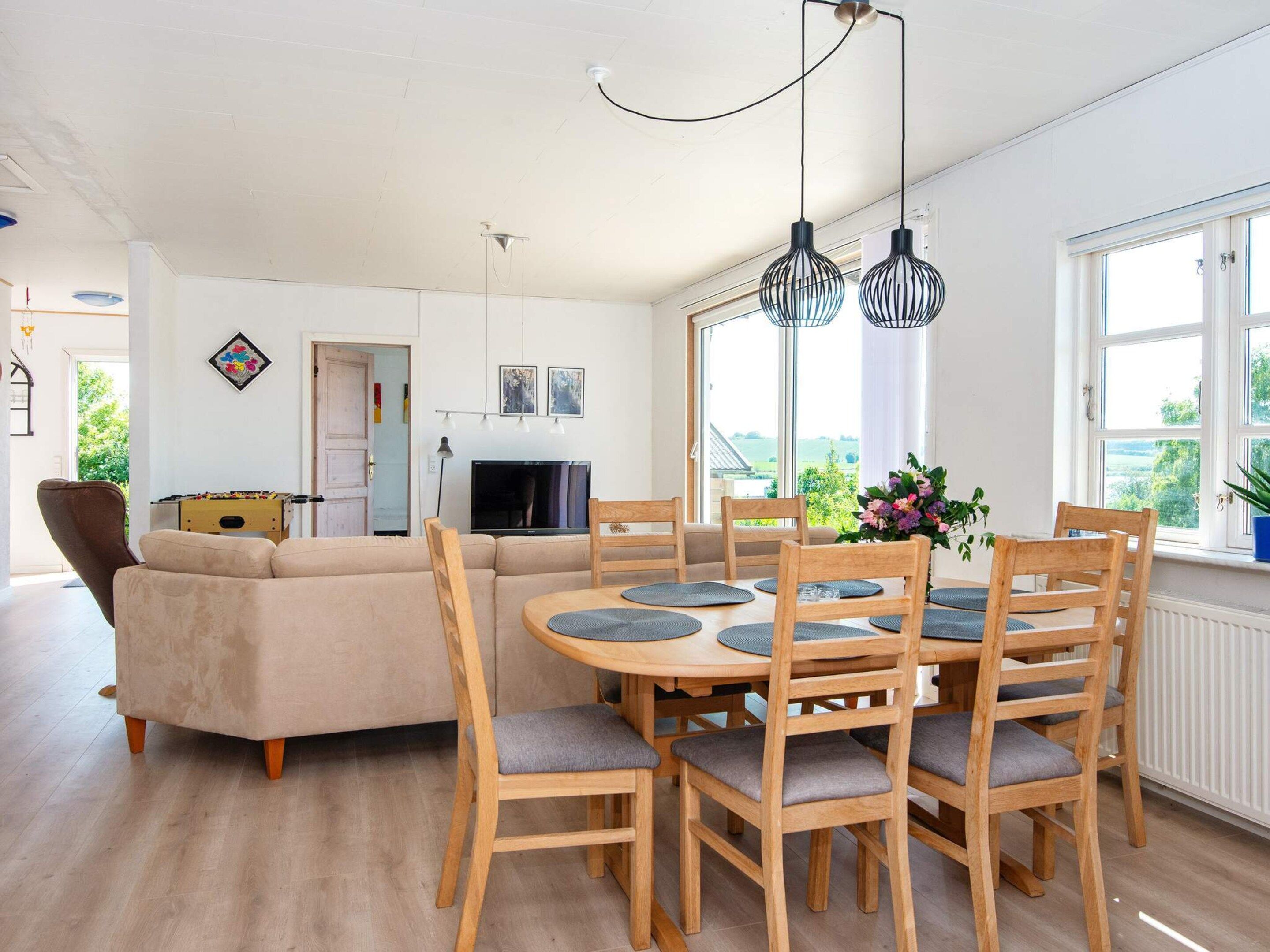 A modern living room with a sofa, a dining table with chairs, a television, and a window with a view.