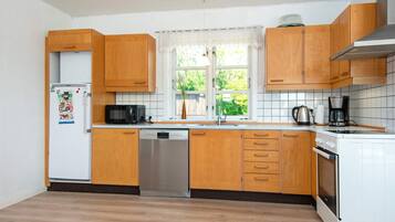 A kitchen with wooden cabinets, a dishwasher, a microwave, a stove, and a window with a view of greenery outside.