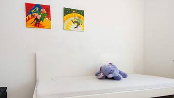 A bedroom with a white bed, a plush toy on the bed, and two colorful paintings on the wall.