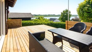 A wooden deck with a table and chairs, overlooking a lake and greenery. - 6 Person Holiday Home in Nordborg (Nordborg)