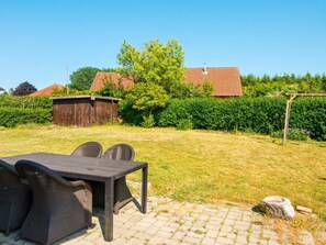 A patio area with a table and chairs, a wooden shed, and a hedge in the background. - 6 Person Holiday Home in Nordborg (Nordborg)