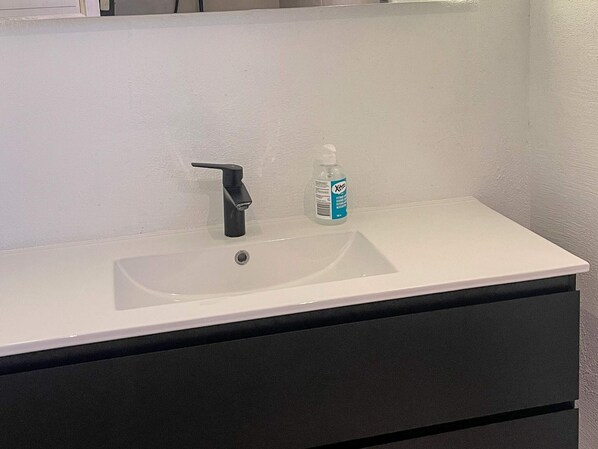 A bathroom with a white sink, black faucet, and a bottle of hand sanitizer. - 6 Person Holiday Home in Nordborg (Nordborg)