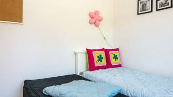 Una cama individual con cabecera acolchada, una almohada y un adorno floral en la pared.