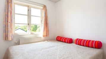Quarto com cama, duas almofadas, janela com cortinas e radiador.