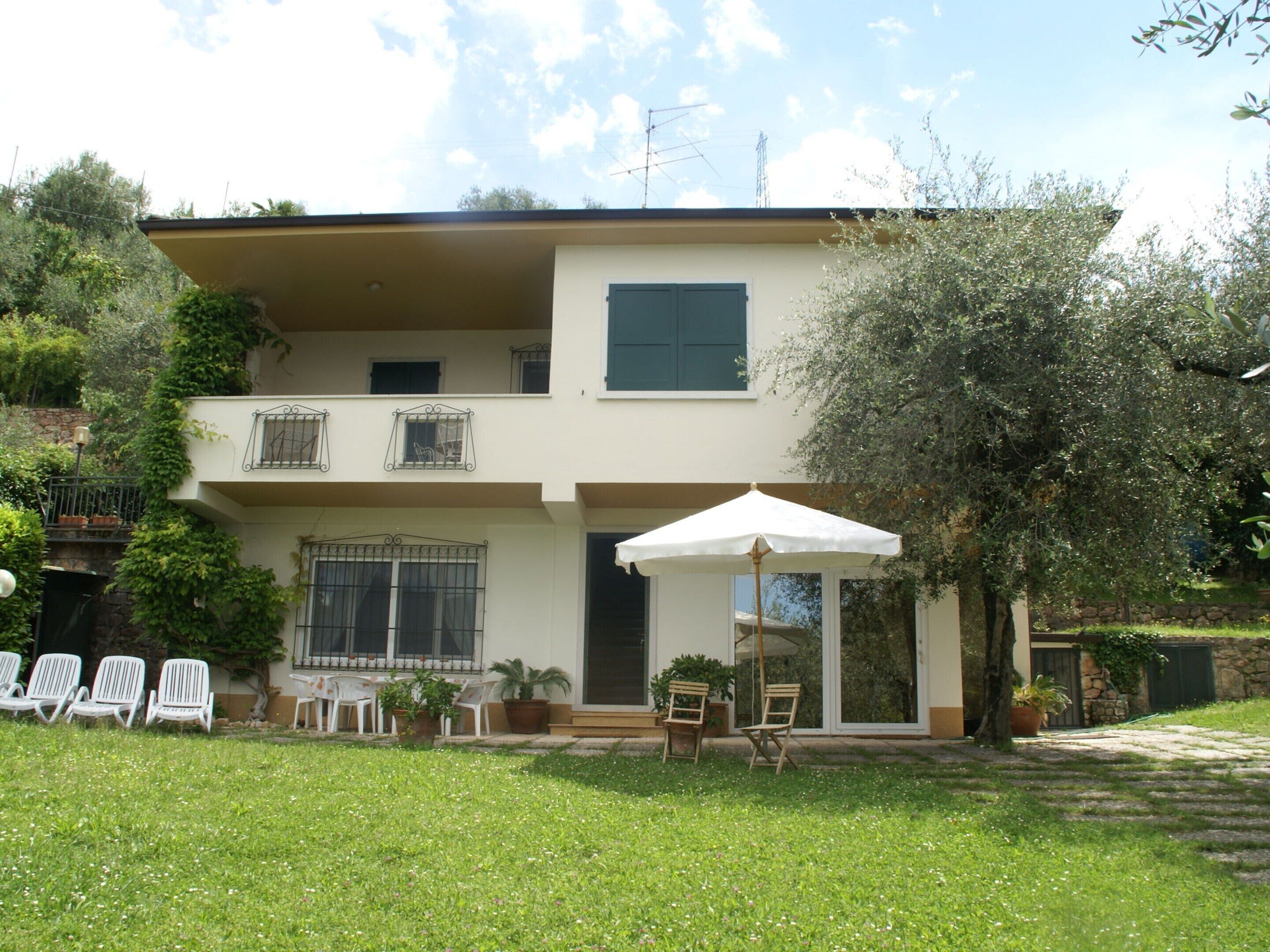 A two-story house with a balcony, outdoor seating, and a large umbrella.