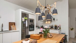 A modern kitchen with white cabinetry, a wooden dining table, and a unique chandelier. - 4 Star Holiday Home in Ebeltoft (Ebeltoft)